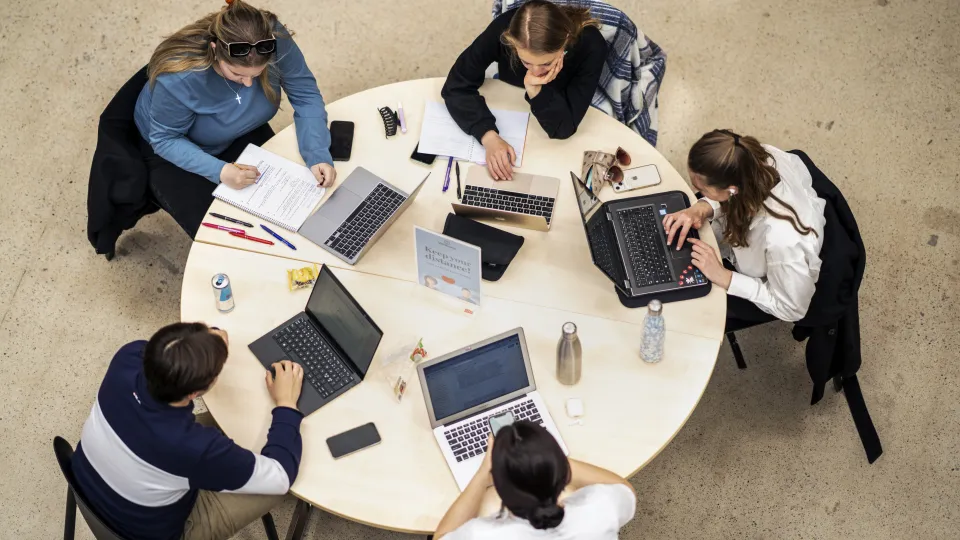 five students studying by a round table with laptops